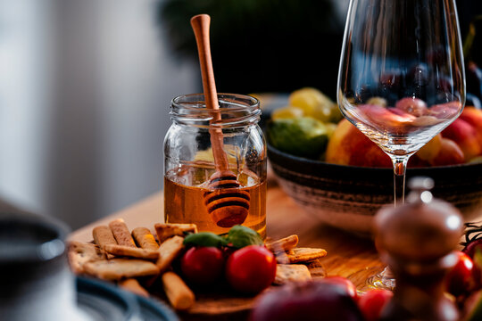 Wine lunch honey jar with wooden dipper on wooden board, gourmet appetizer presentation, cozy autumn dining concept, sweet food pairing detail with crackers and red wine glass setup.