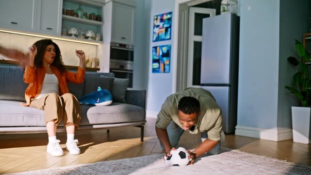 Boy scoring goal home living room. Parents cheering son soccer game indoors.
