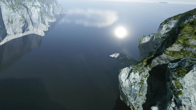 Sunlight illuminates deep blue waters and green clad cliffs, creating a soft reflection on the calm, clear afternoon sea.