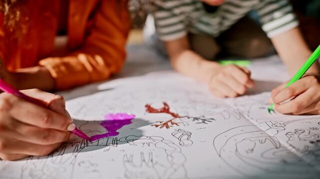 Closeup hands coloring giant paper markers. Family drawing together home floor.