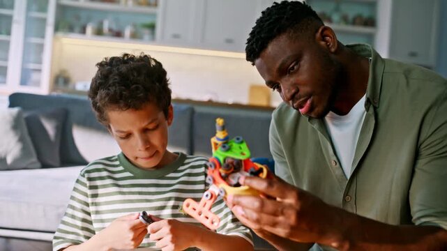 Dad helping boy assemble robot toy home. Father son building construction set.