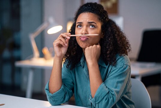 A young woman with a perplexed expression holds a pencil above her upper lip, contemplating a difficult problem in a softly lit office setting.