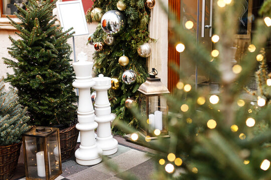 Giant White Chess Pieces standing outside Storefront with Green Garland and Bokeh Lights during Festive Season. xmas outdoor decor