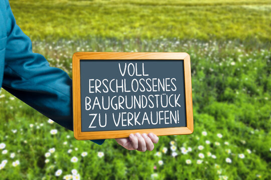 Kreidetafel mit Text "Voll erschlossenes Baugrundst&uuml;ck zu verkaufen" auf einer gr&uuml;nen Wiese