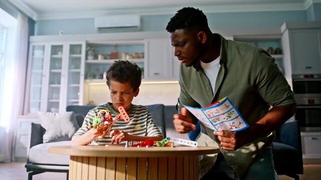 Kid building robot toy with dad reading instruction manual. Happy family home.