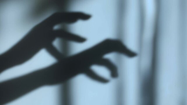Creepy shadow of human hands with bent fingers moving behind a curtain. Dark horror scene with eerie silhouette, suspenseful atmosphere, fear, danger, and mystery. Perfect for themes of horror movies,