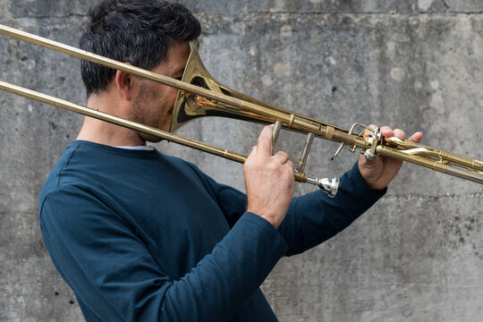 A adult man making a joke while trying to learn how to play the brass trombone by holding it in reverse position outdoors