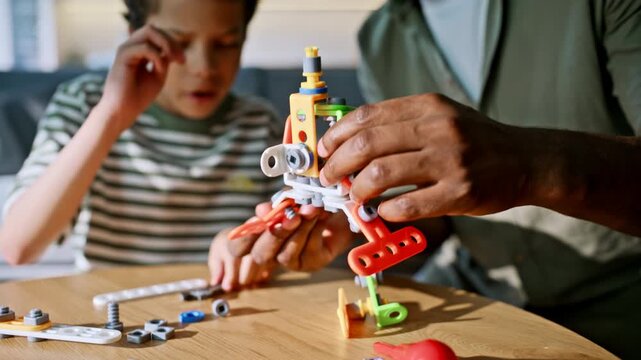Father son building toy construction kit. Closeup hands assembling parts home.