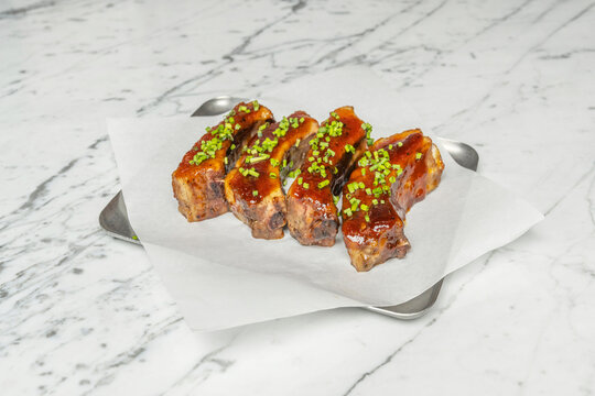 Tender glazed BBQ pork ribs garnished with fresh chopped chives served on parchment paper over a marble surface.