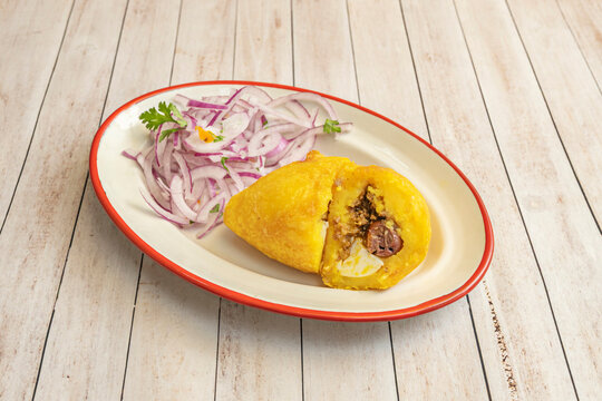 Traditional Peruvian papa rellena stuffed with minced meat, hard-boiled egg, and olives served with pickled red onion salsa.