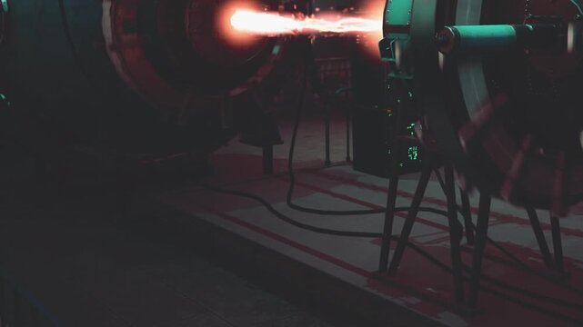 Bright electric sparks fly as two complex machines interact during a high voltage experiment in a dimly lit laboratory.