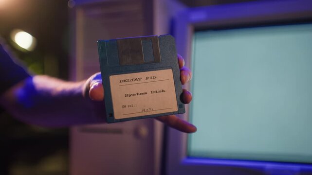 Floppy disk in hand, retro 3.5 inch diskette in front of old computer, vintage 90s data storage, save icon and nostalgia for old technology