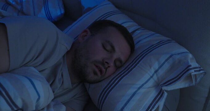 Man talking in his sleep while resting on a pillow in a dark bedroom