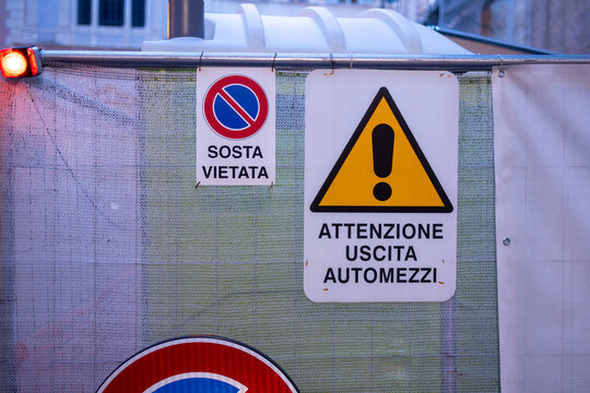 Italian no parking and vehicle exit warning signs on a construction site fence in Rome, Italy