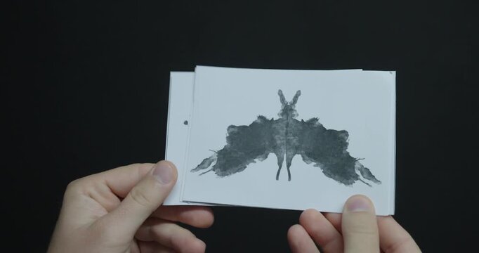 Hands holding a black symmetrical inkblot test card for psychological assessment