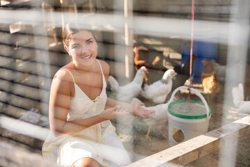 Young woman in dress feeding chickens grain in hen house © JackF