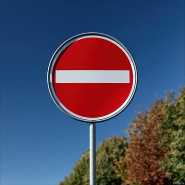 Red circular traffic sign indicating no entry or restricted access mounted on metal pole against clear blue sky and green foliage background in daylight