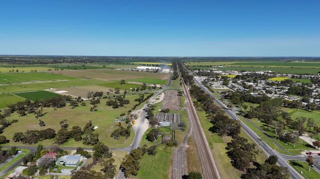 Aerial drone view of dual railway tracks and parallel Dukes Highway through the outskirts of Keith, South Australia, with residential properties, open green paddocks and the flat agricultural plains