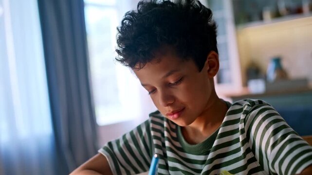 Smiling boy writing notebook home. Mixed race pupil doing homework close up.