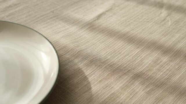 Close-Up of Daylight Shadows Shifting Across a Textured Linen Tablecloth and Ceramic Plate