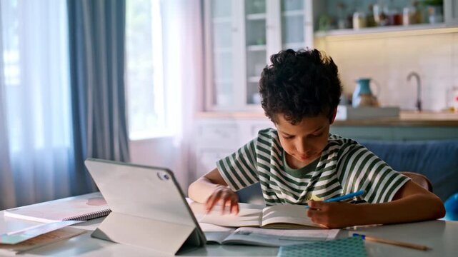 African american kid studying tablet home kitchen. Boy writing notebook lesson.