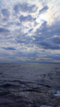 Sunbeams breaking through dark clouds over stormy ocean waves with sun rays on water

