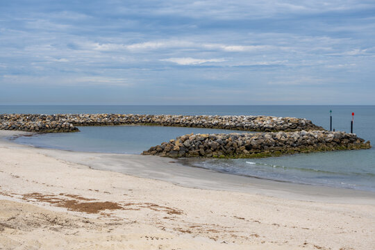 Rock breakwater arms forming a sheltered harbour entrance at West Beach, Adelaide, South Australia, with channel marker poles. Coastal protection and marine infrastructure, safe boating access.