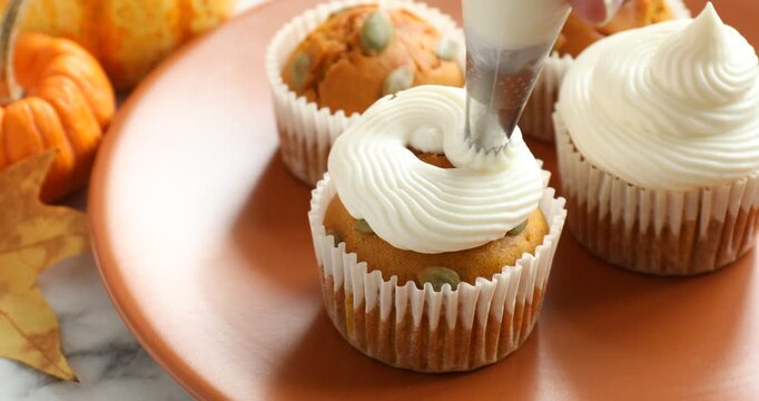 Woman whipping cream onto delicious pumpkin cupcake at white marble table, closeup