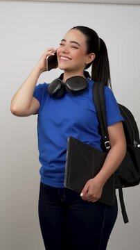 Hispanic college student talking on smartphone holding laptop