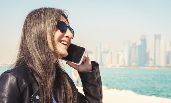 Portrait Young modern traveler woman chat using smartphone esim data coverage with West Bay skyline background Corniche waterfront. Roaming internet communication technology roaming lifestyle vacation