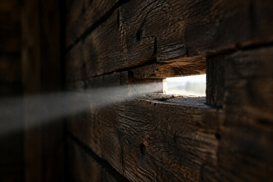 Close-up of a narrow arrow slit in a wooden wall, a single beam of light shining through, detailed wood.