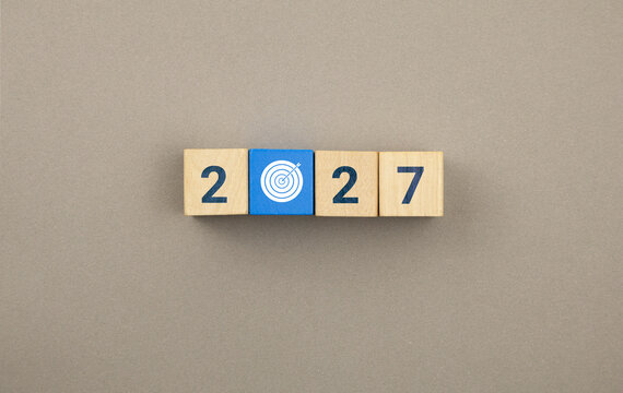 A concept featuring stacked wooden cubes, an arrow icon, and a target. Represents objectives, strategy, financial planning, and risk management for the new year 2027.