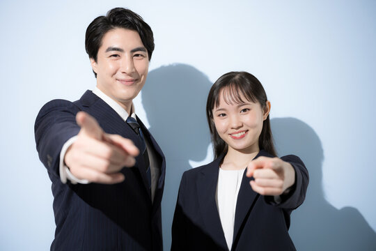 [水色背景ビジネス]ネイビーのスーツを着て笑顔で並ぶ20代と30代の日本人男女、カメラ目線リクルート　指をさして目標を目指すやno1や選ぶ「君だ！」のイメージ