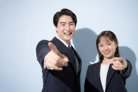 [水色背景ビジネス]ネイビーのスーツを着て笑顔で並ぶ20代と30代の日本人男女、カメラ目線リクルート　指をさして目標を目指すやno1や選ぶ「君だ！」のイメージ