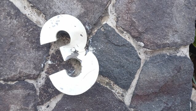 Close-up photo of a rustic  house number plate with the number 3, mounted on a stone wall in Jakarta.