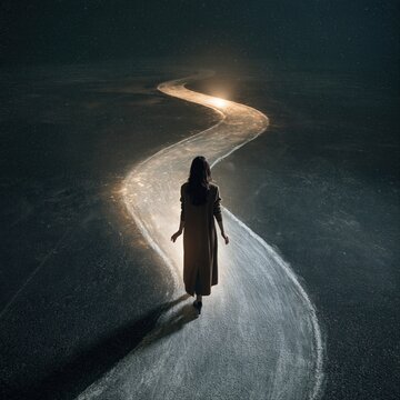 A lone woman in a long dress walks along a glowing winding path toward a distant light across a dark, starry landscape.