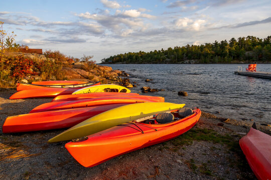 Vibrant kayaks line the shore of Killarney Channel, Ontario at sunset, creating a picturesque scene with calm waters and lush greenery.