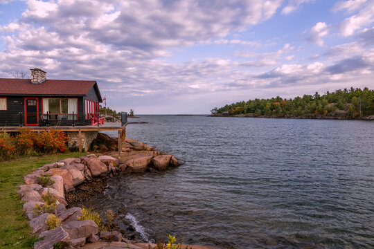 Rocky shoreline of Killarney Channel in Ontario, looking towards Georgian Bay at sunset, with a charming lakeside cabin and scenic sky.