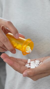 close up woman hand holding a medicine, with pours the pills out of the yellow orange medicine bottle. Stop drug use Taking Medication Caring for the health care medical concept.