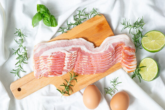 Fresh raw sliced pork belly or bacon on a wooden cutting board with eggs and limes