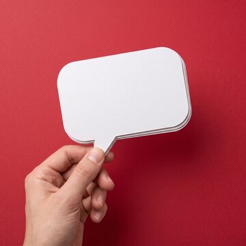 Hand holding blank white speech bubble cutout on solid red background surface