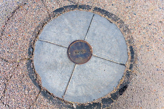 Top-down close-up view of a round concrete utility structure surrounding a small circular rusty metal water valve cover