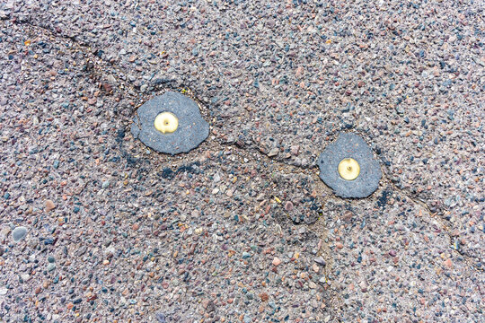 Close-up of two circular golden metal survey markers embedded in asphalt pavement along a crack in the road