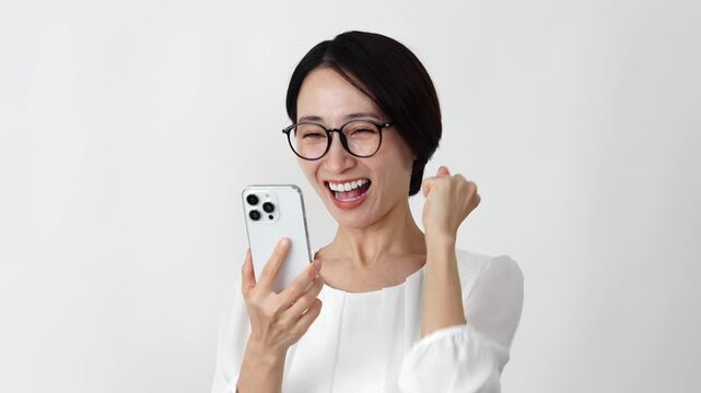スマホを持ってガッツポーズをするミドル女性　白背景　スローモーション