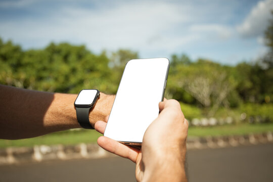 Person using smartphone with smartwatch on wrist in natural setting