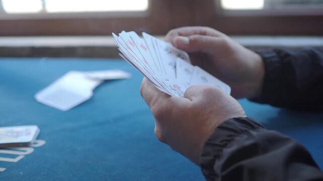 Player shuffles a hand of playing cards at a table during a card game
