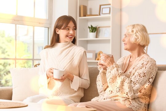 Intergenerational connection and family bonding, young woman and senior mother talking while drinking tea on a sofa in a bright living room interior
