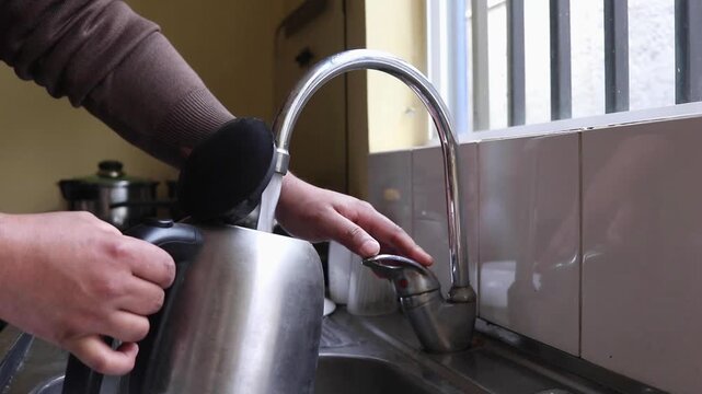 Horizontal stock video of person filling electric kettle with tap water at kitchen sink