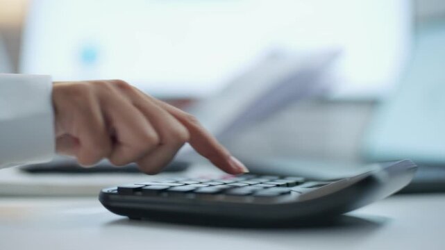 Close up side view of an office worker pressing calculator buttons with financial paperwork in the background, illustrating accounting and cost estimation.