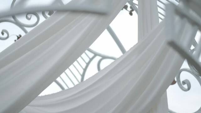 Flowing white fabric draped elegantly across a white metal outdoor gazebo or event arch